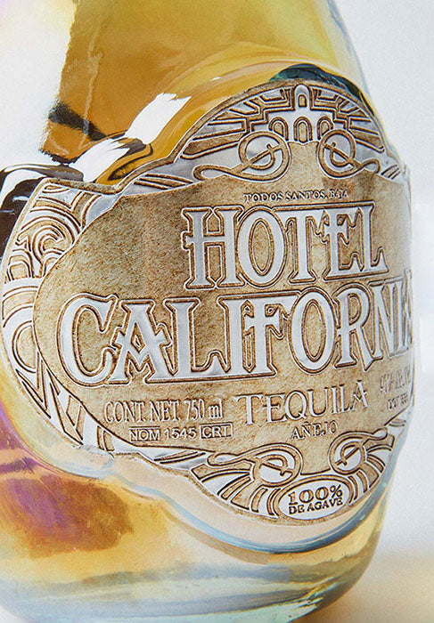 Bottle of Hotel California Añejo Tequila. A premium, craft tequila honoring generations of tequila making tradition, the land from which it comes and the community of artists and craftsman that make it. 100 percent Blue Weber Agave. Jalisco, Mexico 